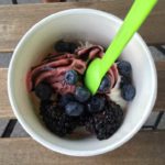 Cup of frozen yogurt with blueberries and bright green spoon