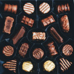 square, rectangular, and round chocolates displayed in repeating pattern on a black background