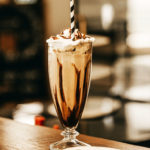 Chocolate milkshake with whip cream and a stripped straw on a counter